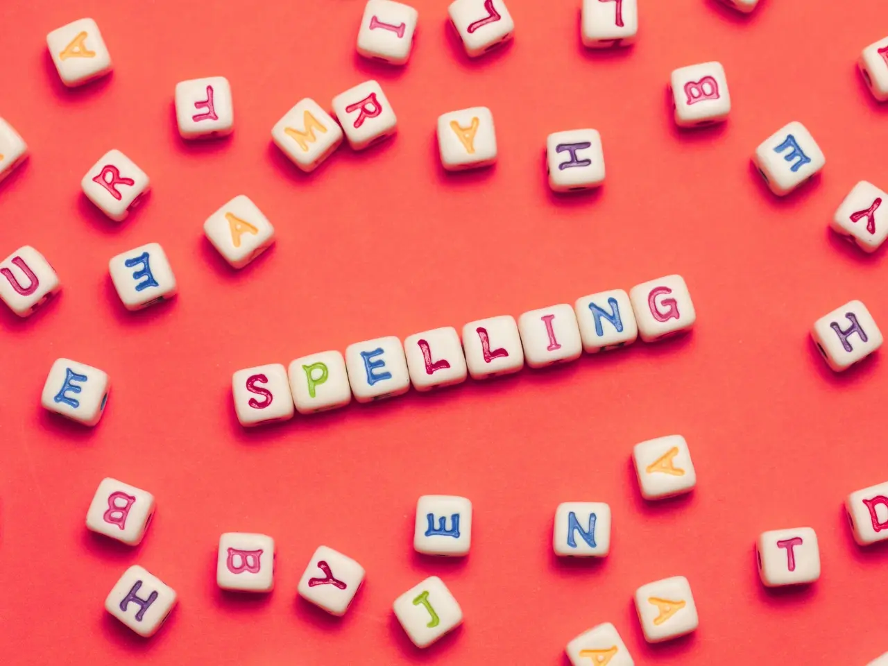 The word “spelling” spelled out with colourful letter cubes on a red background, symbolizing differences in Canadian and British spelling.