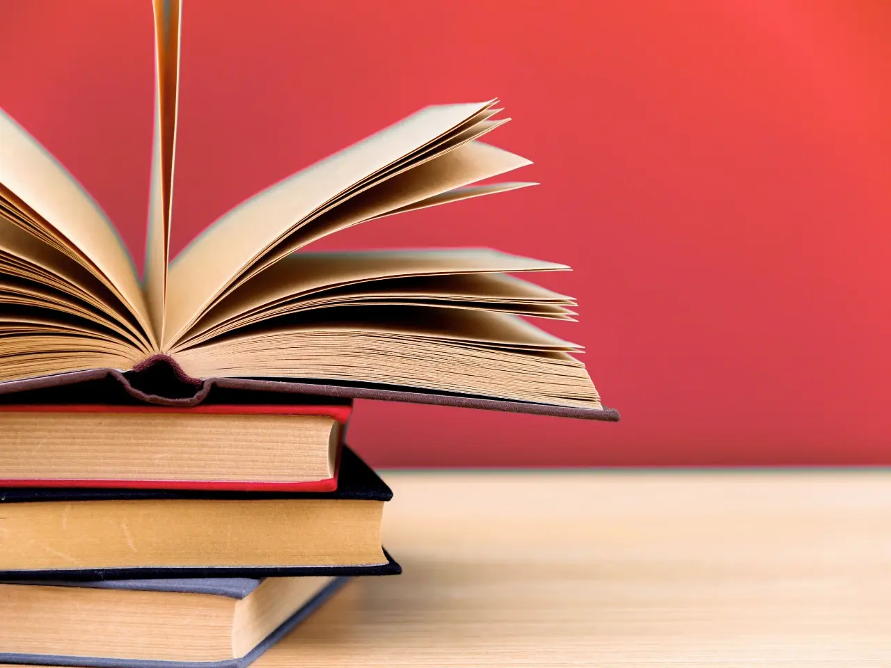 Open book on a stack of books, representing differences in grammar, spelling, and vocabulary between Canadian and British English.