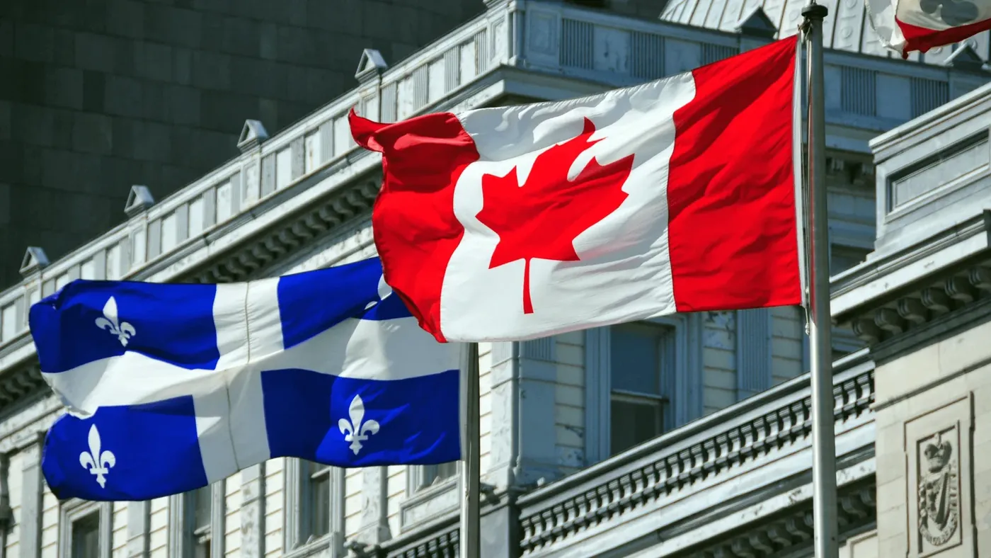 Canadian and Quebec flags waving in front of a government building, symbolizing bilingualism and Quebec’s language laws.