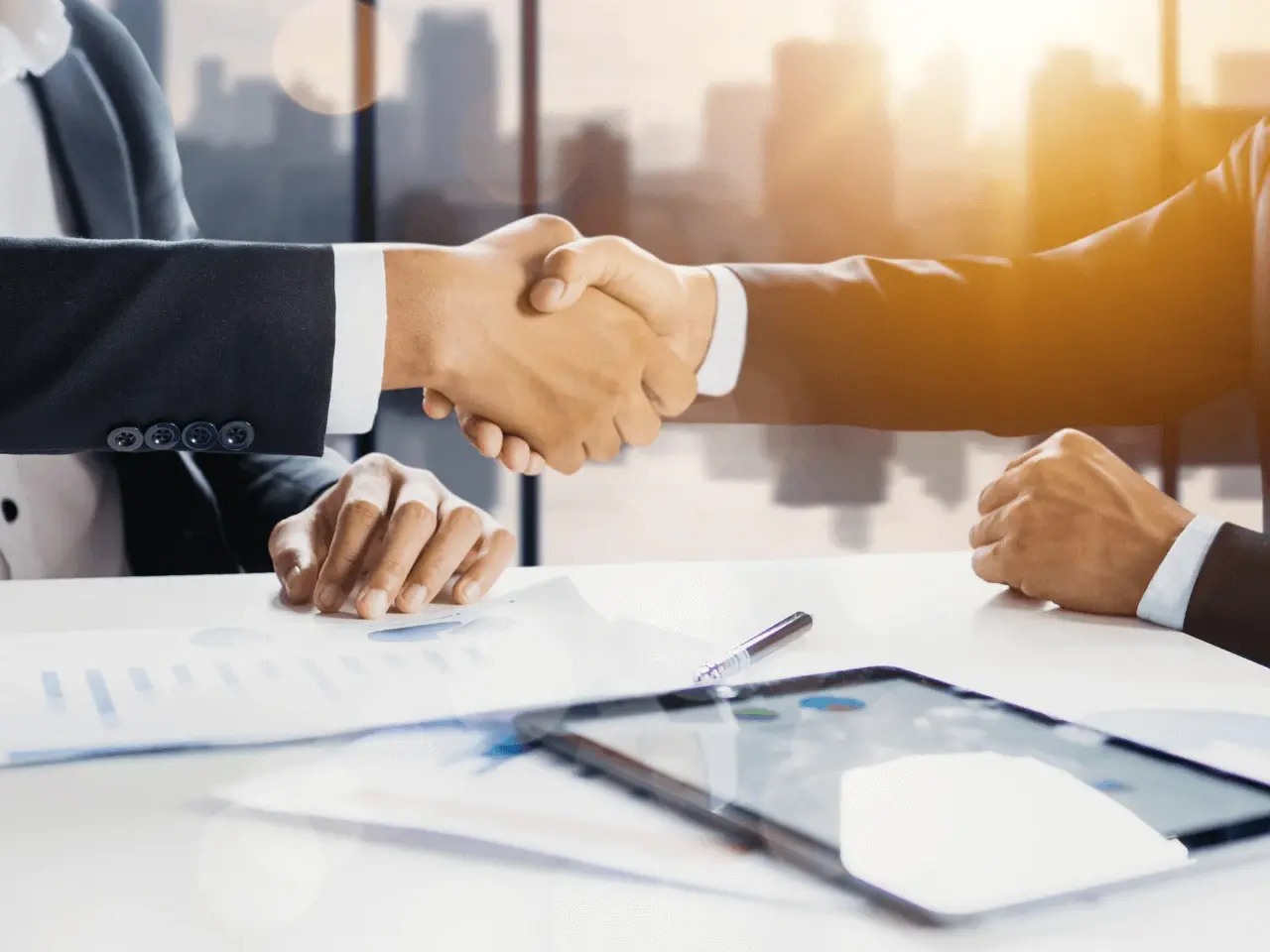 Business professionals shaking hands over documents and a digital tablet, symbolizing agreements and compliance in Quebec language laws.