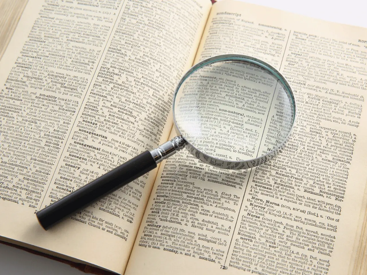 Magnifying glass placed on an open dictionary, symbolizing detailed word analysis and challenges in machine translation accuracy.