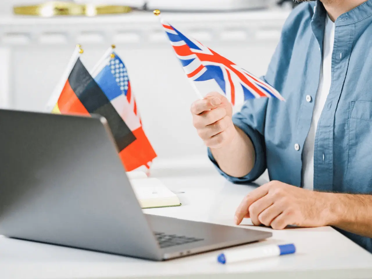 Person holding a UK flag at a desk with a laptop and other international flags, representing multilingual communication.