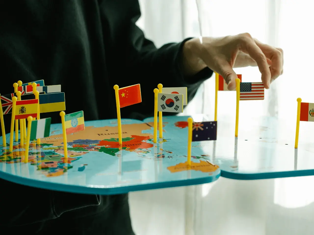 Hand placing small international flags on a world map, symbolizing global markets and multilingual marketing strategies.
