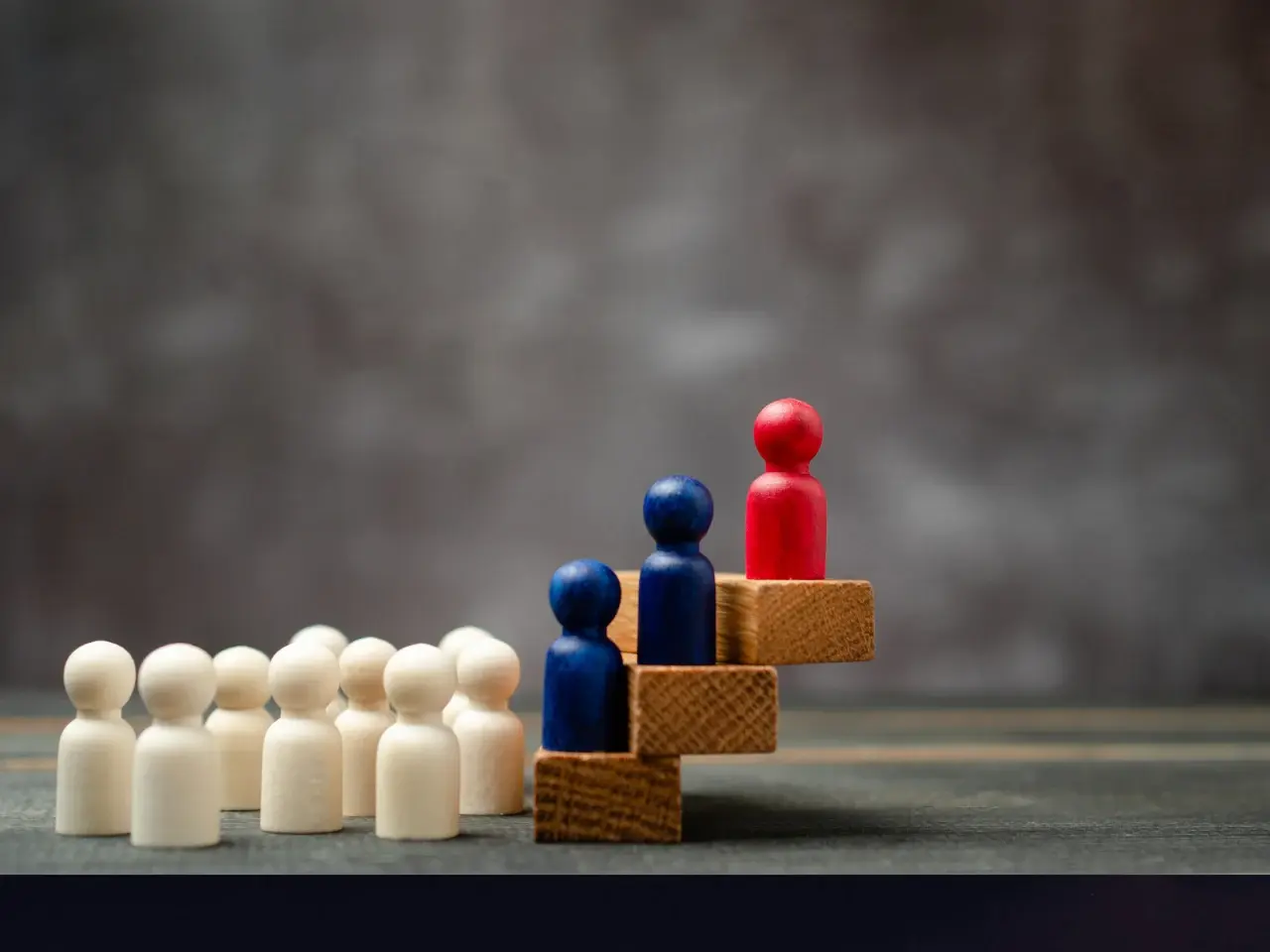 Wooden figures showing a group of people, with blue and red figures standing on steps, symbolizing differences and influence between Canadian French and European French under English impact.