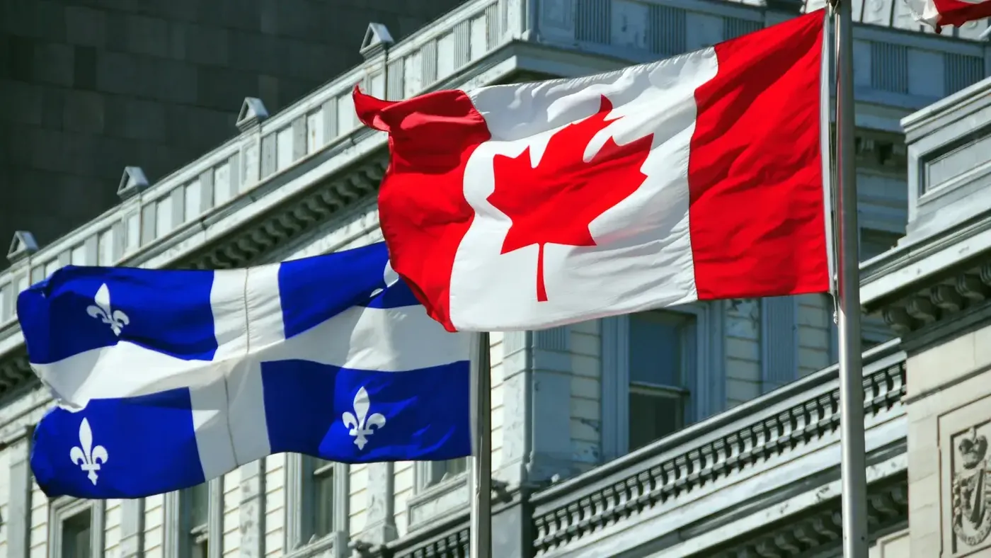 Canadian and Quebec flags flying side by side in front of a government building, symbolizing Quebec language laws and compliance requirements.