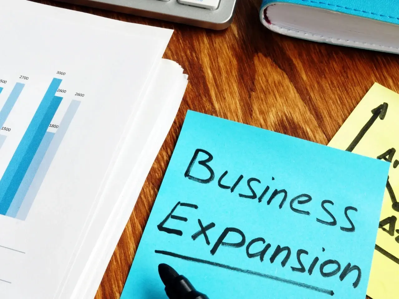 Close-up of a desk with a bar chart report and a blue sticky note that says “Business Expansion,” symbolizing the benefits of localization for business growth.